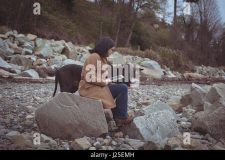 Side view of woman holding digital tablet by dog at beach Stock Photo