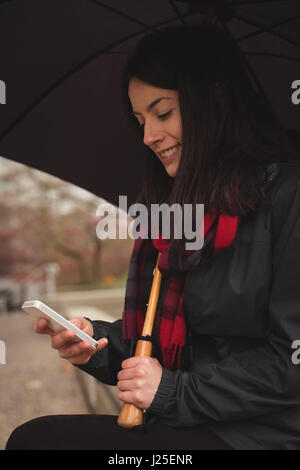 Smiling woman using mobile phone while holding umbrella Stock Photo