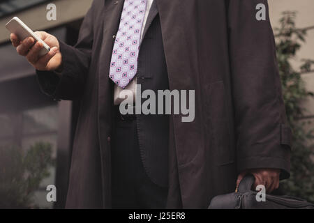 Midsection of businessman using smart phone while standing against building Stock Photo
