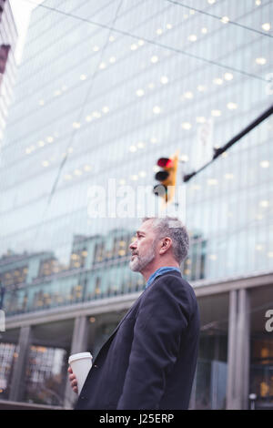 Side view of thoughtful businessman holding disposable glass while standing outside office building Stock Photo