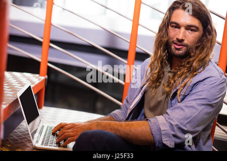 Portrait of sound engineer using laptop on stairs in office Stock Photo