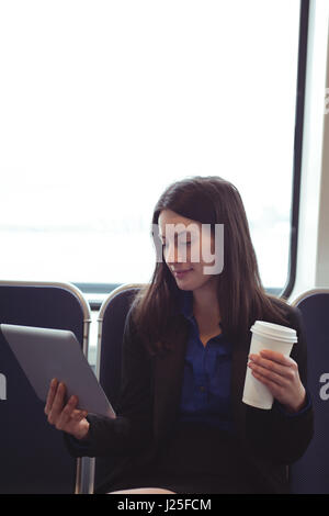 Woman using smart phone and holding coffee cup while sitting in train Stock Photo