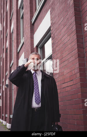 Businessman drinking coffee while standing by building in city Stock Photo