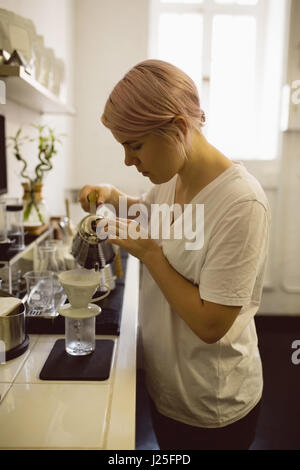 Female barista pouring hot water through funnel in coffee shop Stock Photo