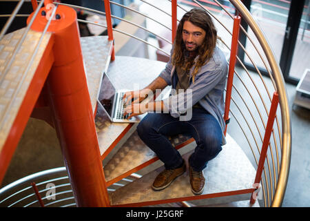 Portrait of sound engineer using laptop on stairs in office Stock Photo