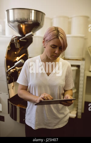 Female barista using digital tablet while standing besides coffee grinding machine in coffee shop Stock Photo