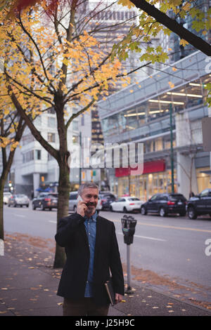 Businessman using smart phone while standing on sidewalk in city Stock Photo