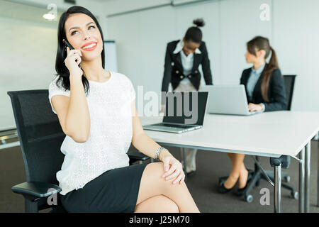 Beautiful businesswomen in an office working on a laptop and calling potential partners Stock Photo