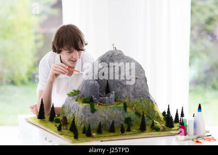 Teenager working on model building school project. Kids build miniature scale model mountain for geography class in high school. Extracurricular activ Stock Photo