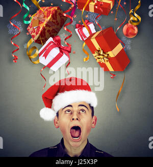 Surprised man in santa claus hat looking up at multiple christmas gifts falling down Stock Photo