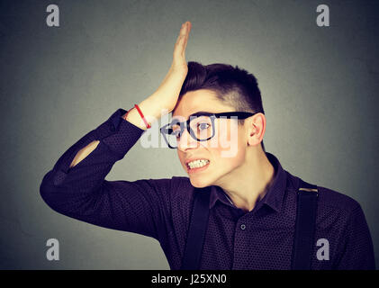 Regrets wrong doing. Silly young man, slapping hand on head having duh moment isolated on gray background. Negative human emotion facial expression fe Stock Photo