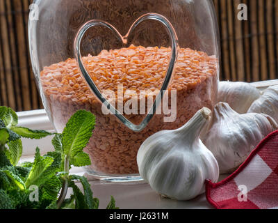 HEALTHY FOOD & jar with heart motif containing Red Lentils, a healthy edible pulse Legume, with garlics and sprig of mint by open kitchen window Stock Photo
