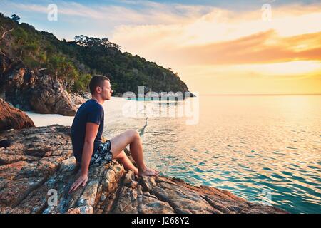 Contemplation at the sunset. Alone young man on the beautiful sand beach. Stock Photo