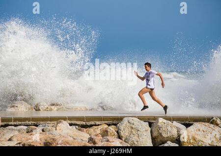 Excited boy on pier running away from splashing water on pier, young boy, teenage, teenager, Spain. Stock Photo