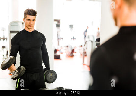 Young muscular man working out in a gym and lifting weights with his reflection showing in a mirror Stock Photo