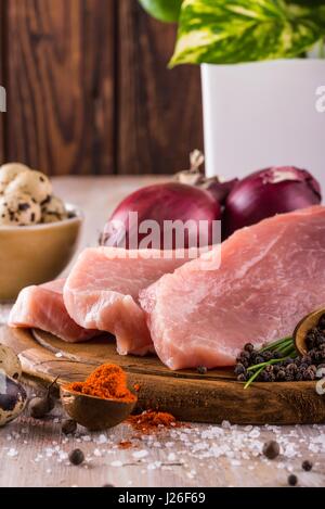 Vertical photo of three slices of raw pork meat which are placed on dark wooden board with whole pepper, milled red capsicum, few pieces of quail eggs Stock Photo
