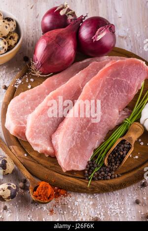 Vertical photo of three slices of raw pork meat which are placed on dark wooden board with whole pepper, milled red capsicum, few pieces of quail eggs Stock Photo