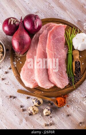Vertical photo of three slices of raw pork meat which are placed on dark wooden board with whole pepper, milled red capsicum, few pieces of quail eggs Stock Photo