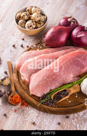 Vertical photo of three slices of raw pork meat which are placed on dark wooden board with whole pepper, milled red capsicum, few pieces of quail eggs Stock Photo
