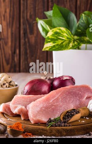 Vertical photo of three slices of raw pork meat which are placed on dark wooden board with whole pepper, milled red capsicum, few pieces of quail eggs Stock Photo