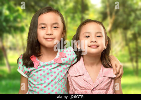 Funny two little sisters standing and hugging on the park Stock Photo