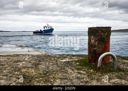 A small passenger motor boat approaches a slipway under grey skies toward a post and eyelet to tying off. Stock Photo