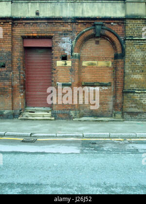 old abandoned brick building with shutter and bricked up doorway and pavement Stock Photo