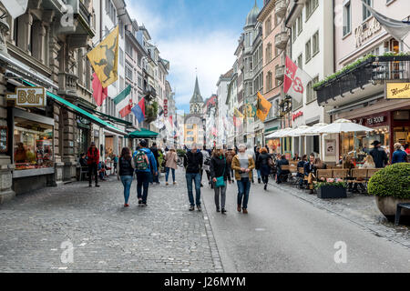 ZURICH, SWITZERLAND - MAY 14, 2016: People on shopping street Rennweg with boutique shops, flags on old buildings and St. Peter church clock tower in  Stock Photo