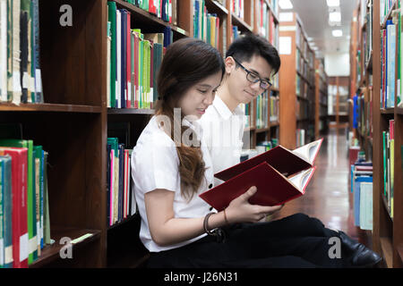 Portrait of Asian couple students studying in library. Asian couple students reading book together. Stock Photo