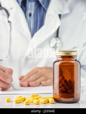 Yellow pills on doctor desk, doctor writing prescription in background Stock Photo