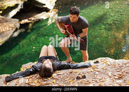 Young man serenading his girlfriend by a stream Stock Photo