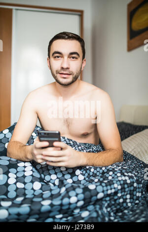 Man lying in morning bed with phone using app or reading news feed Stock Photo