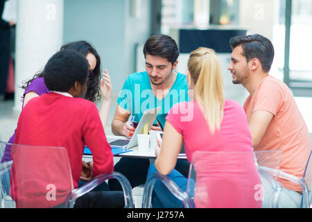 A group of teenagers sitting at the table in cafe, using laptop and drinking orange juice. Stock Photo