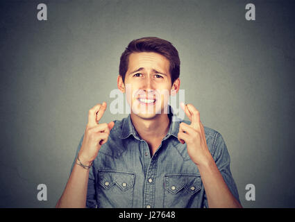 Young man making a wish keeping his fingers crossed isolated on gray wall background. Waiting for special moment Stock Photo