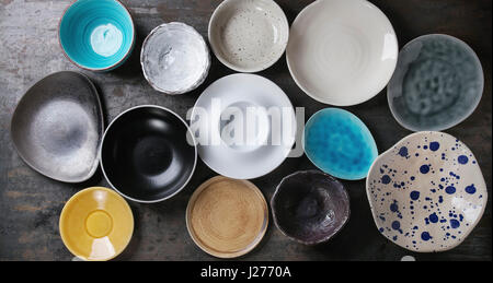 Empty colorful modern ceramic plates and bowls collection. Various of dishware over dark metal background. Top view Stock Photo