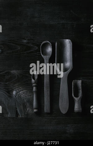 Black burnt wooden empty kitchenware cutting board, plates, scoop and spoon over black wood background. Flat lay with space Stock Photo