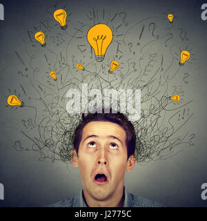Surprised man with many ideas light bulbs above head looking up isolated on gray wall background. Eureka creativity concept Stock Photo