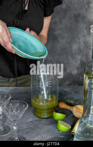 A women is preparing a matcha wine cocktail. Photographed from front view on a grey background. Stock Photo