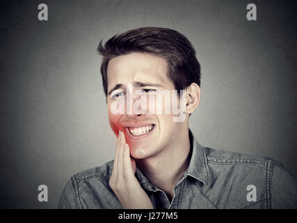 Closeup portrait young man with sensitive toothache crown problem about to cry from pain touching outside mouth with hand isolated on gray background. Stock Photo