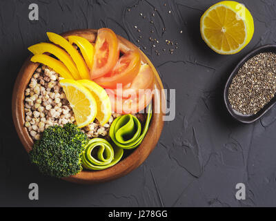 Top view of vegetarian buddha bowl with green buckwheat, broccoli, avocado, tomatoes and yellow sweet pepper paprika on dark concrete background with  Stock Photo