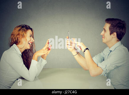 Young man and woman sitting at table using mobile phones, texting via social networks with obsessed expression or taking pictures of each other Stock Photo