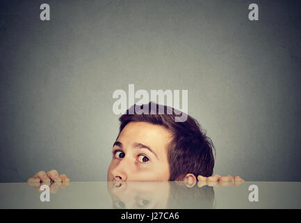 suspicious scared man peeking from under the table hiding Stock Photo