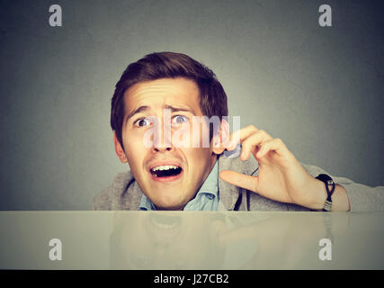 Funny scared man peeking from behind the desk isolated on gray background Stock Photo