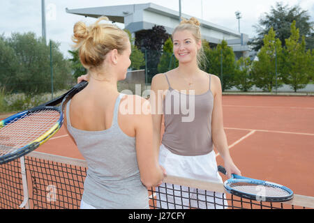 Women shaking hands over tennis court net Stock Photo