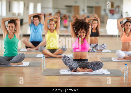 Young curly female instructor doing yoga exercises with group in gym Stock Photo