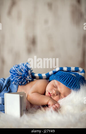 newborn baby sleeps on a white blanket, he is only 13 days old, baby wearing a white knitted cap Stock Photo
