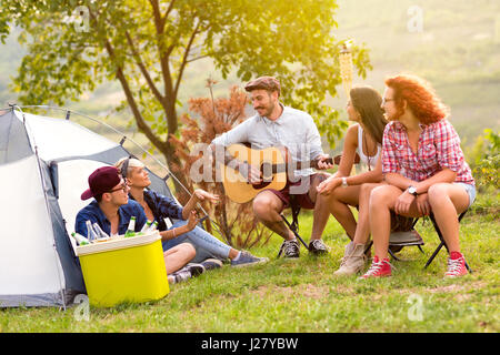 Cheerful guys with guitar in front  in camp in wood Stock Photo