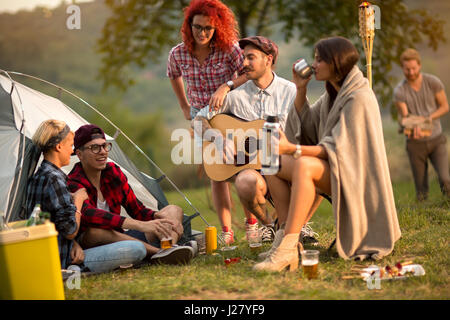 Girls and guys socializing on sunset in camp in nature Stock Photo