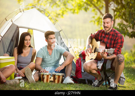 young friends playing drums and guitar front tent on camping trip Stock Photo