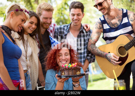 Curly birthday girl is very happy with her friends and birthday chocolate cake on birthday celebration in nature Stock Photo